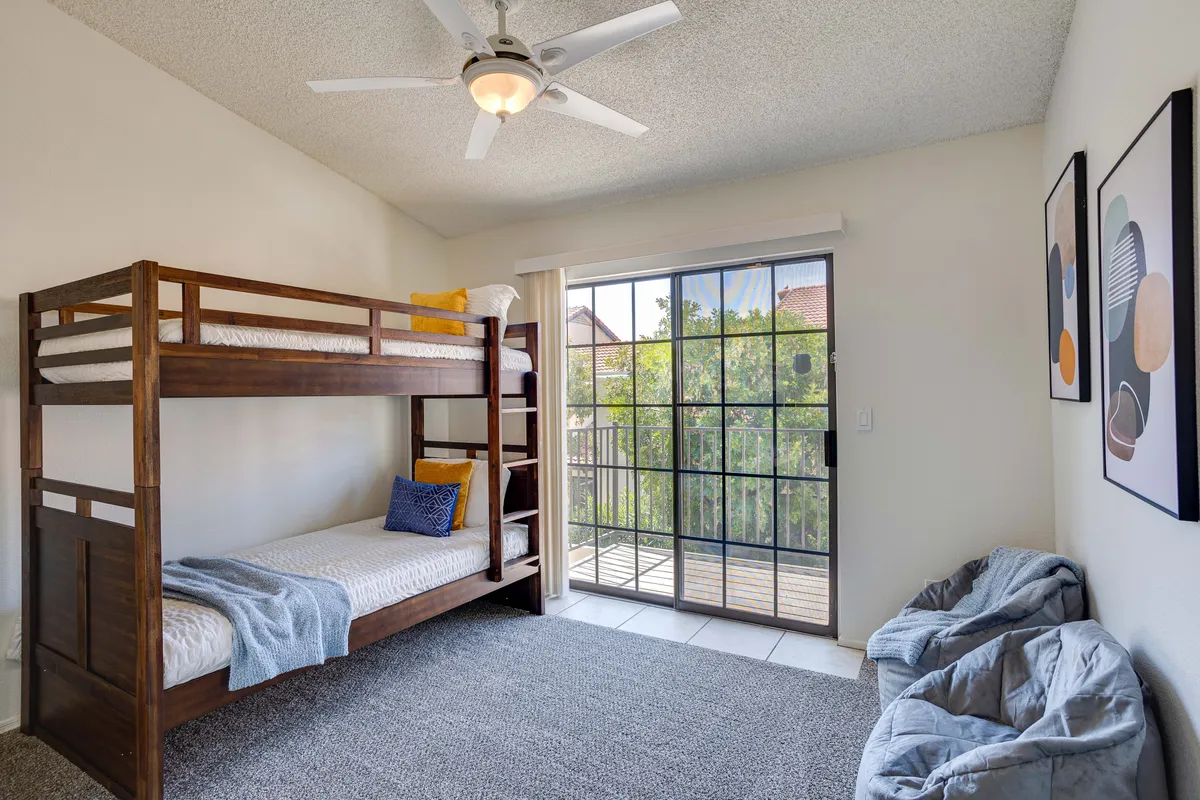A playful children's bunk room with a bunk bed, a sliding glass door letting in natural light, and charming decorative artwork. The environment feels lively yet relaxed, inviting kids to play, read, and unwind.