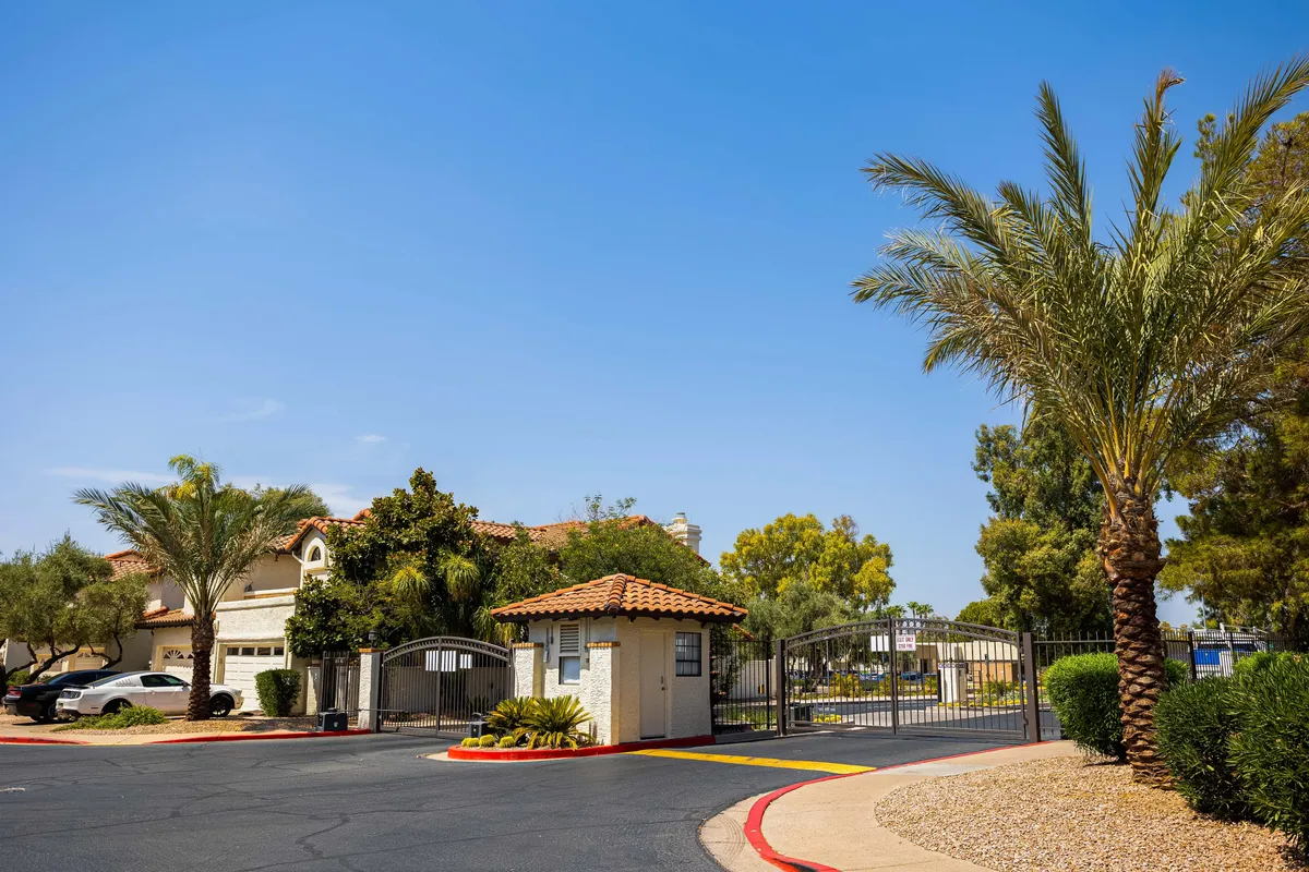 A secure gated entrance framed by palm trees and well-maintained landscaping, with a driveway leading toward the home. The scene exudes a sense of safety and community.