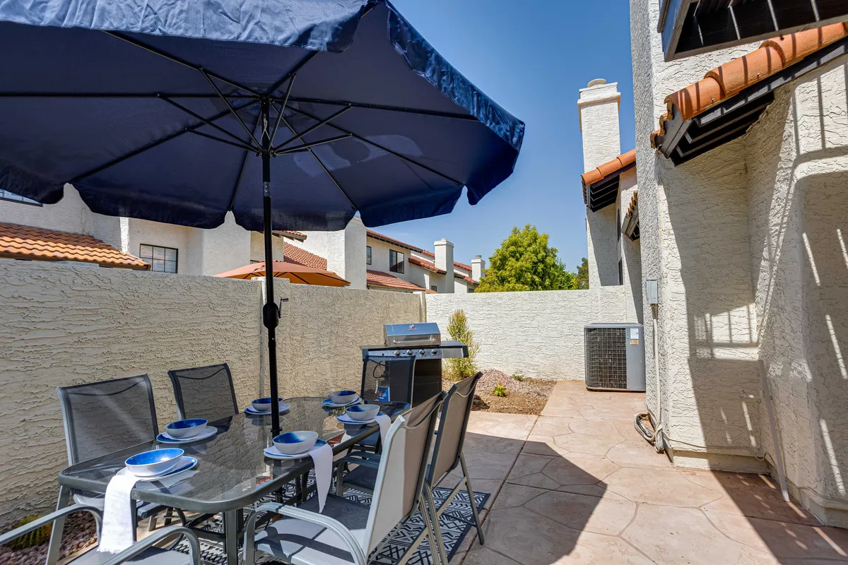 An outdoor dining area with a large umbrella and grill, surrounded by comfortable chairs, sets the stage for memorable meals and gatherings. The inviting setup highlights the possibilities for socializing and enjoying the Arizona climate.