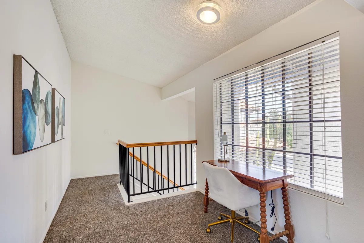 A light and productive workspace nook featuring a desk by a window, inspirational artwork, and a staircase leading to other areas. The mood is serene and conducive to focused work or creative thinking.