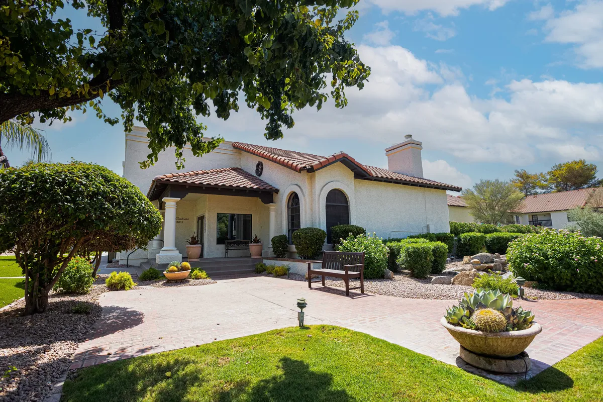 A welcoming front porch featuring decorative planters, a cozy bench, and a stone pathway, all framed by manicured greenery. The space exudes tranquility, inviting residents and guests to relax and socialize outdoors.