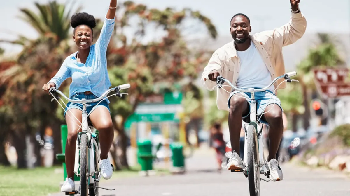 Two cyclists ride along a palm-lined, well-maintained pathway, emphasizing an active, outdoor lifestyle. The image evokes a sense of playfulness and community, showcasing local recreation and the convenience of exploring the neighborhood by bike.
