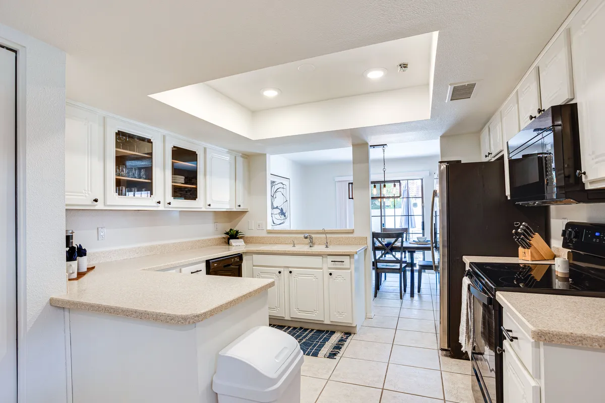 A view through the remodeled kitchen highlights gleaming white cabinetry, a spacious kitchen island, and modern stainless steel appliances. The dining area is visible through the window, reinforcing the connection between kitchen and dining, and inviting culinary creativity and family gatherings.