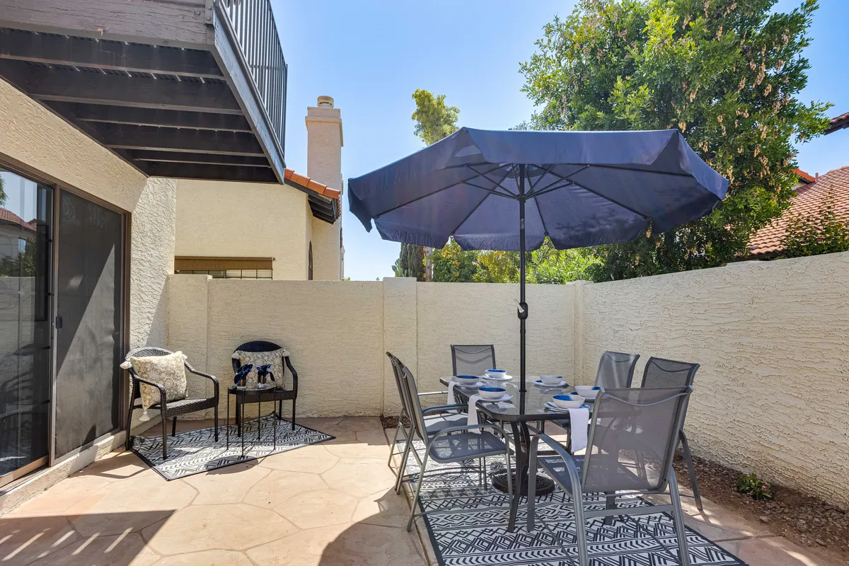 The backyard setup features an outdoor dining table with a large umbrella and decorative rug, surrounded by chairs. The area is casual and inviting, perfect for al fresco dining or relaxed morning coffee, with the south-facing aspect allowing for bright, sunny gatherings.