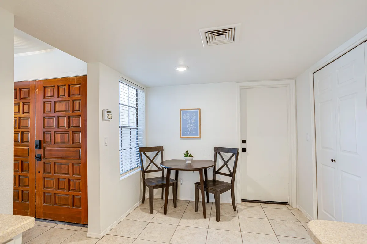 This image focuses on a stylish wooden front door leading into a cozy interior area with a round dining table and two chairs. The door hints at the private entry while the scene demonstrates an easy flow from the entrance to the heart of the home.