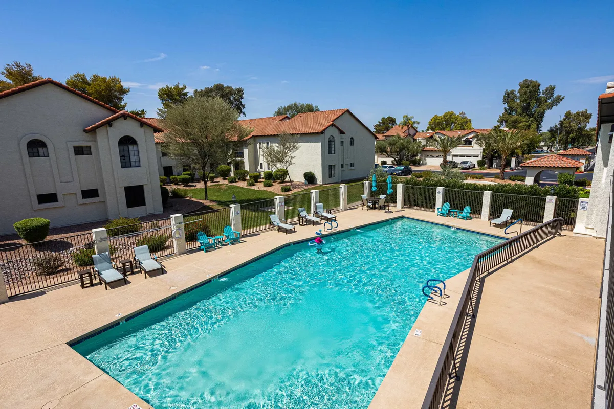 A sparkling swimming pool is surrounded by comfortable lounge chairs and lush landscaping, creating a serene and inviting setting for relaxation or socializing. The scene is vibrant yet tranquil, suggesting resort-style amenities and leisure time after a busy day.